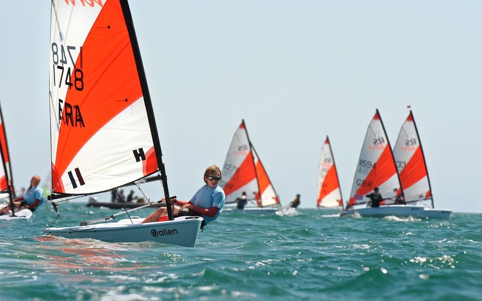 A group of people are sailing in the ocean and one of the sails has the number 11 on it