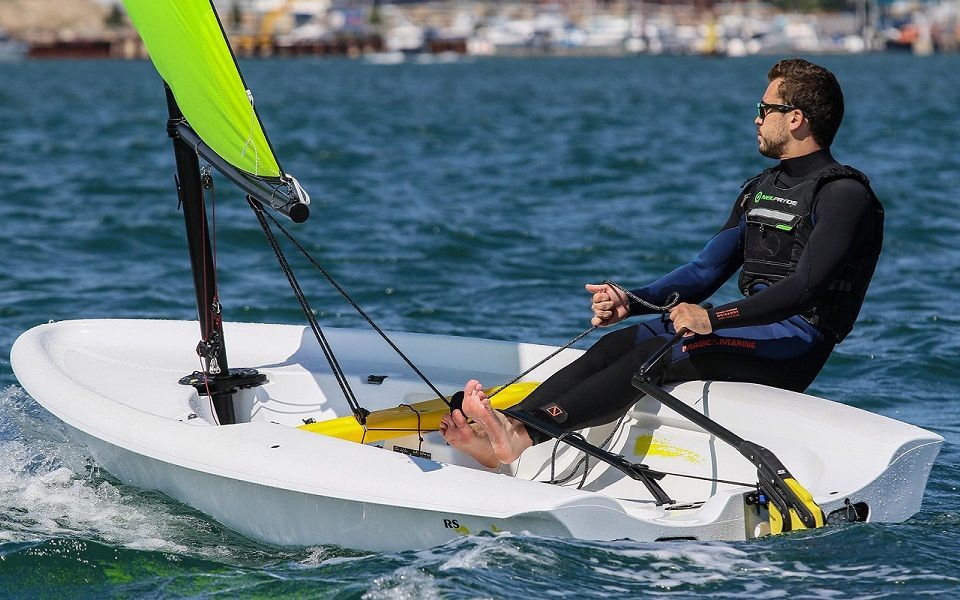 A man is sitting on a small sailboat in the water.