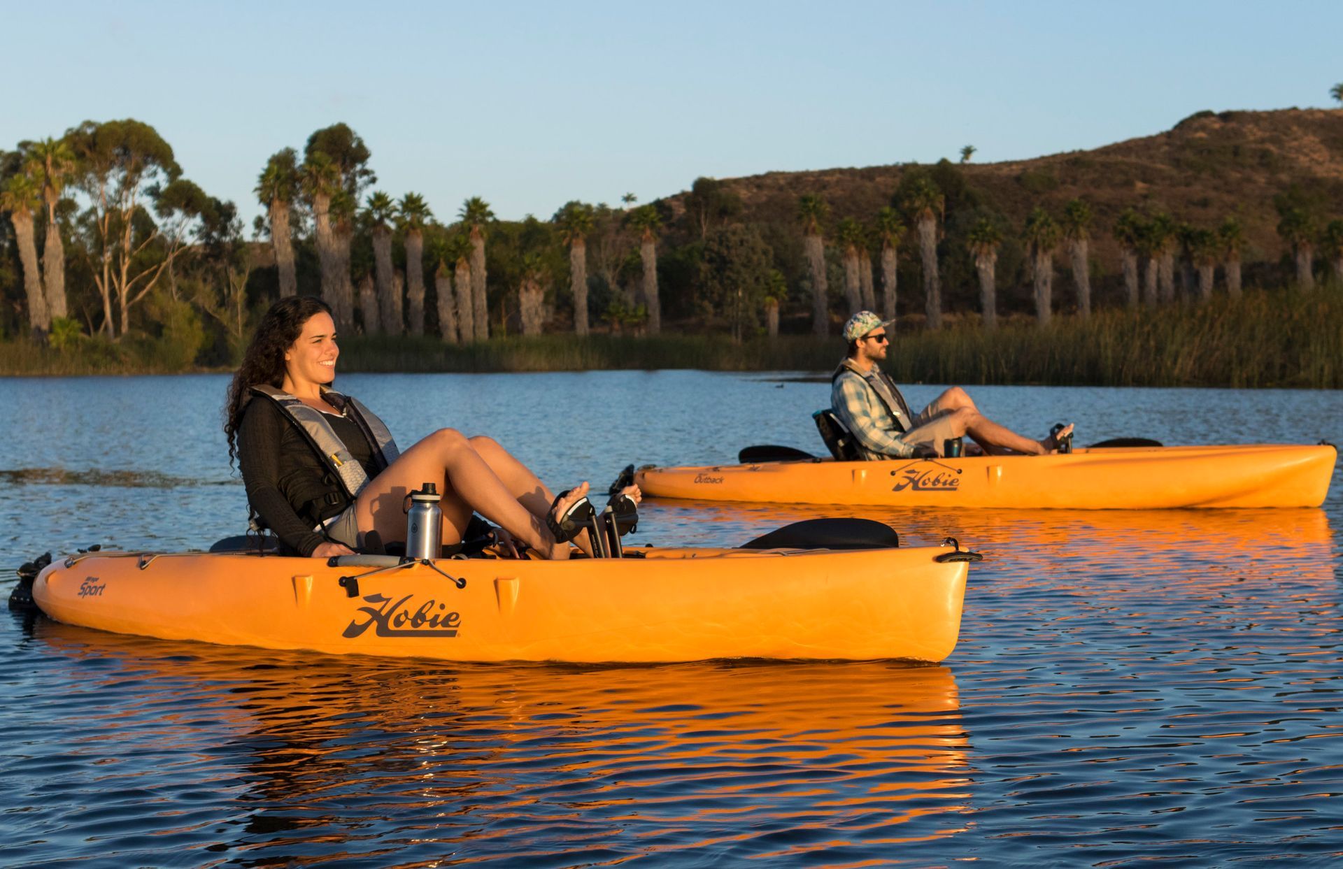 Two people are sitting in orange kayaks on a lake.