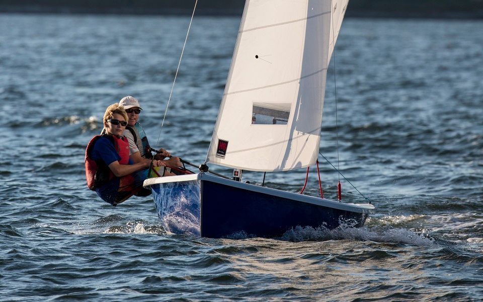 Two people are sailing a small boat on a lake.