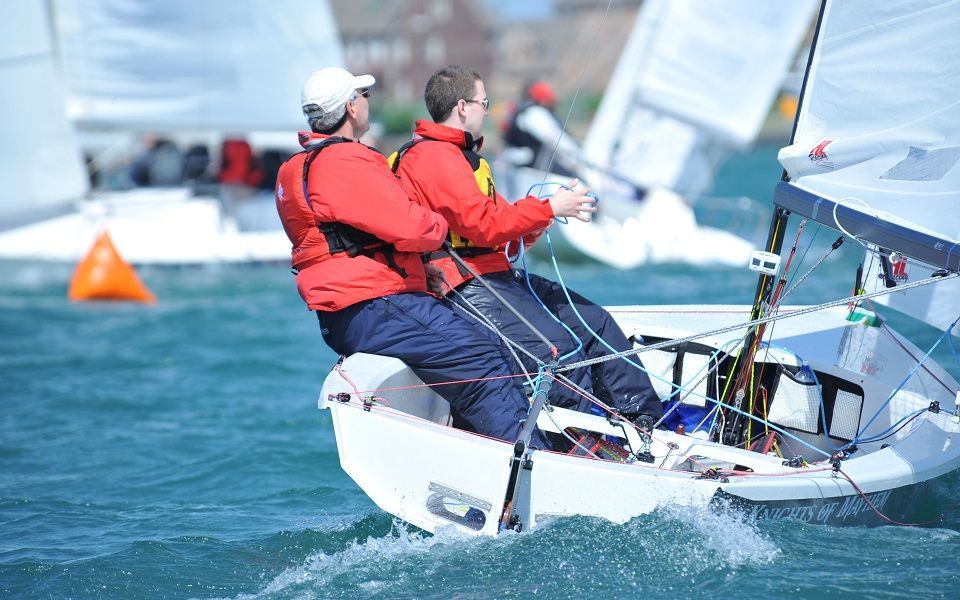 Two men are riding on the back of a sailboat in the water.