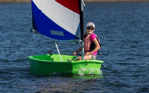 A young girl is sailing a small green boat on a lake.