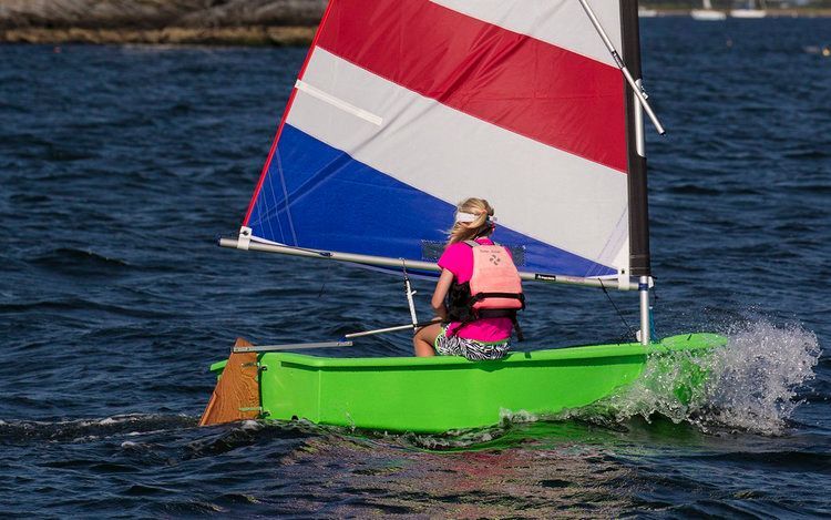 A person is riding a green sailboat in the water.
