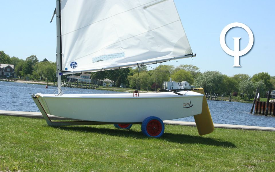 A small sailboat is sitting on the grass near a body of water