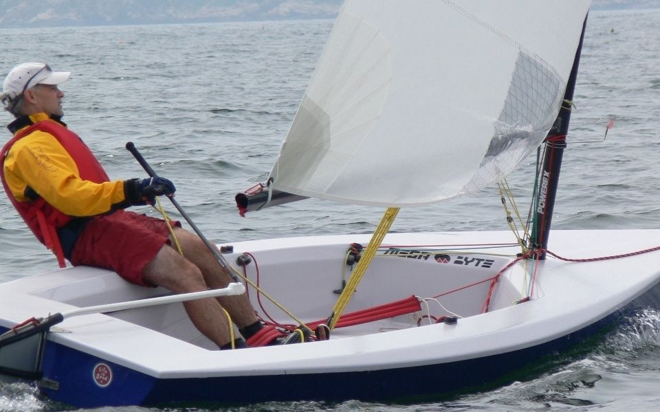 A man in a yellow vest is sailing a small sailboat
