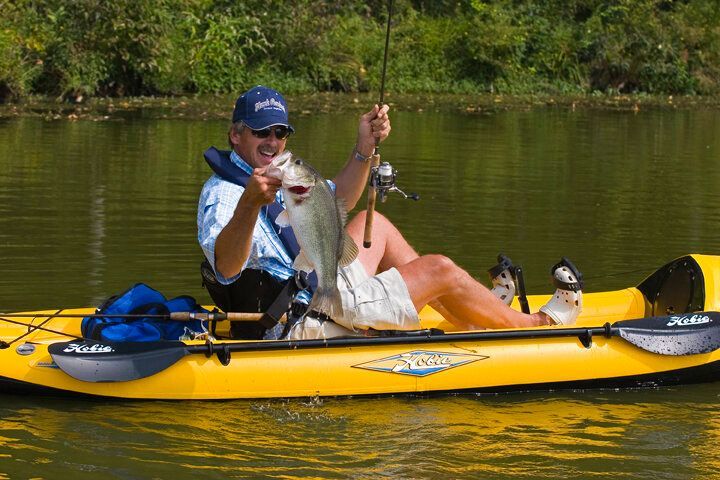 A man is sitting in a yellow kayak holding a fish.