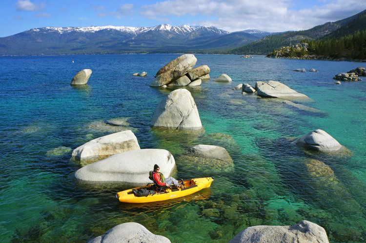 A person is in a yellow kayak in a lake surrounded by rocks.