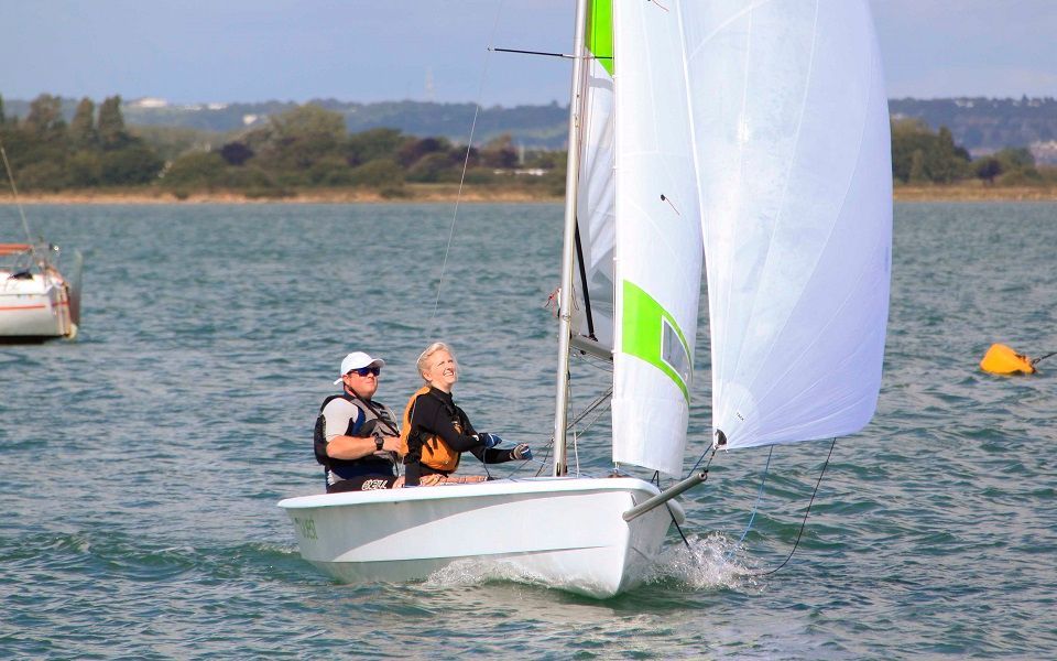 Two people are sailing a small boat on a lake.