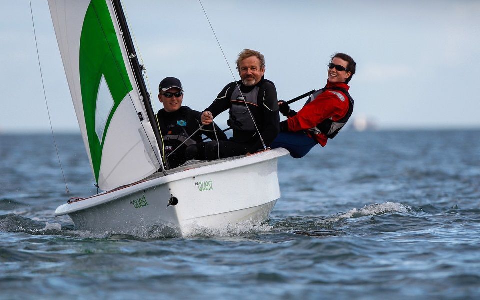 Three men are sailing a small boat in the ocean.