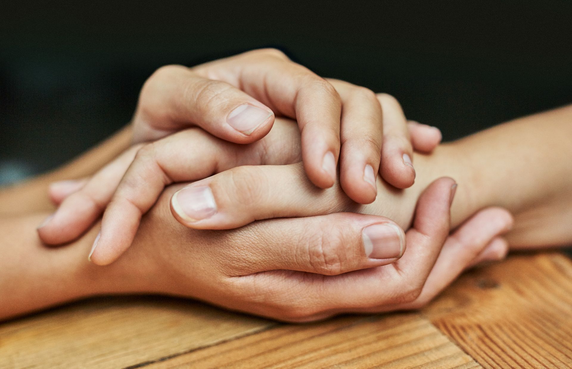 Two people are holding hands on a wooden table.