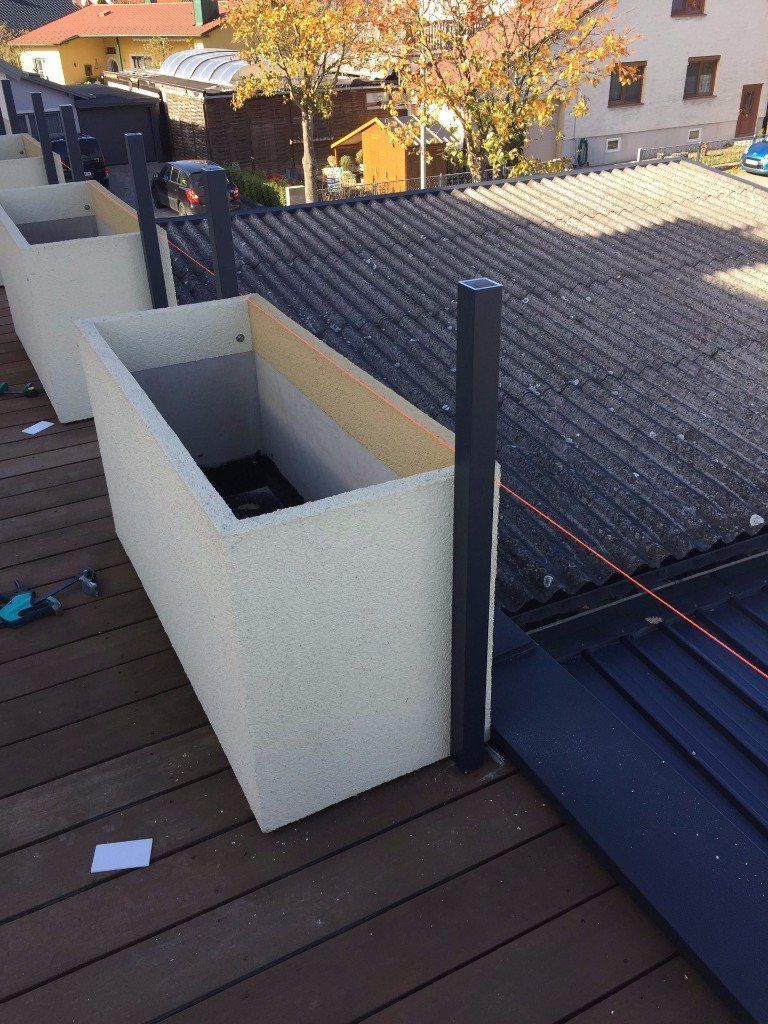 Eine Reihe von Pflanzgefäßen steht auf einem Holzdeck.