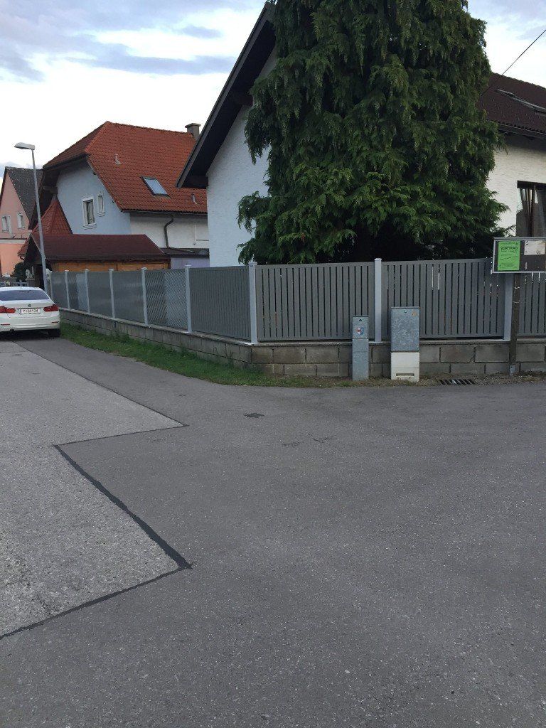 Ein weißes Auto steht am Straßenrand neben einem Zaun