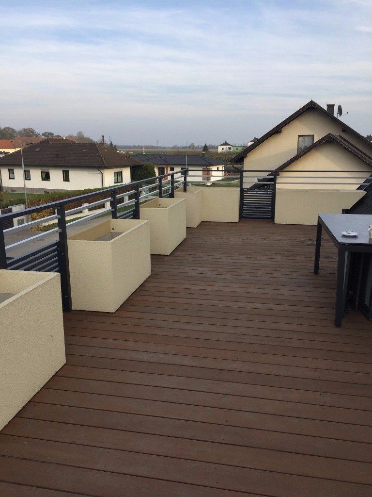 Ein Holzdeck mit Pflanzkübeln und einem Tisch darauf