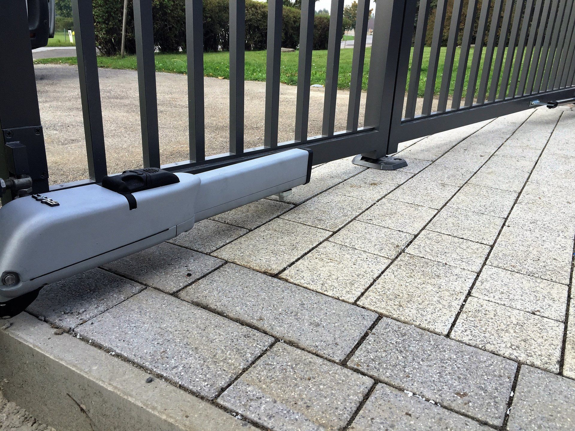 Auf einem gepflasterten Gehweg steht ein Tor mit einem daran befestigten Motor.