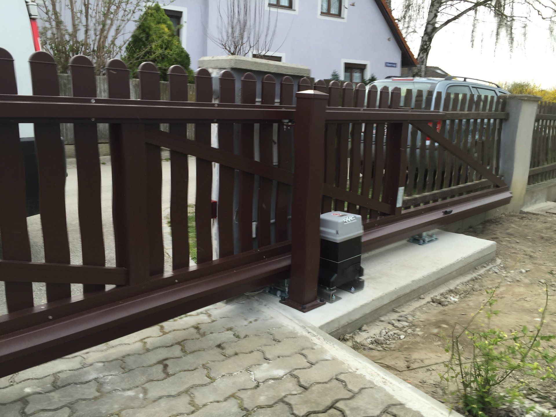 Ein brauner Zaun mit einem Schiebetor vor einem Haus