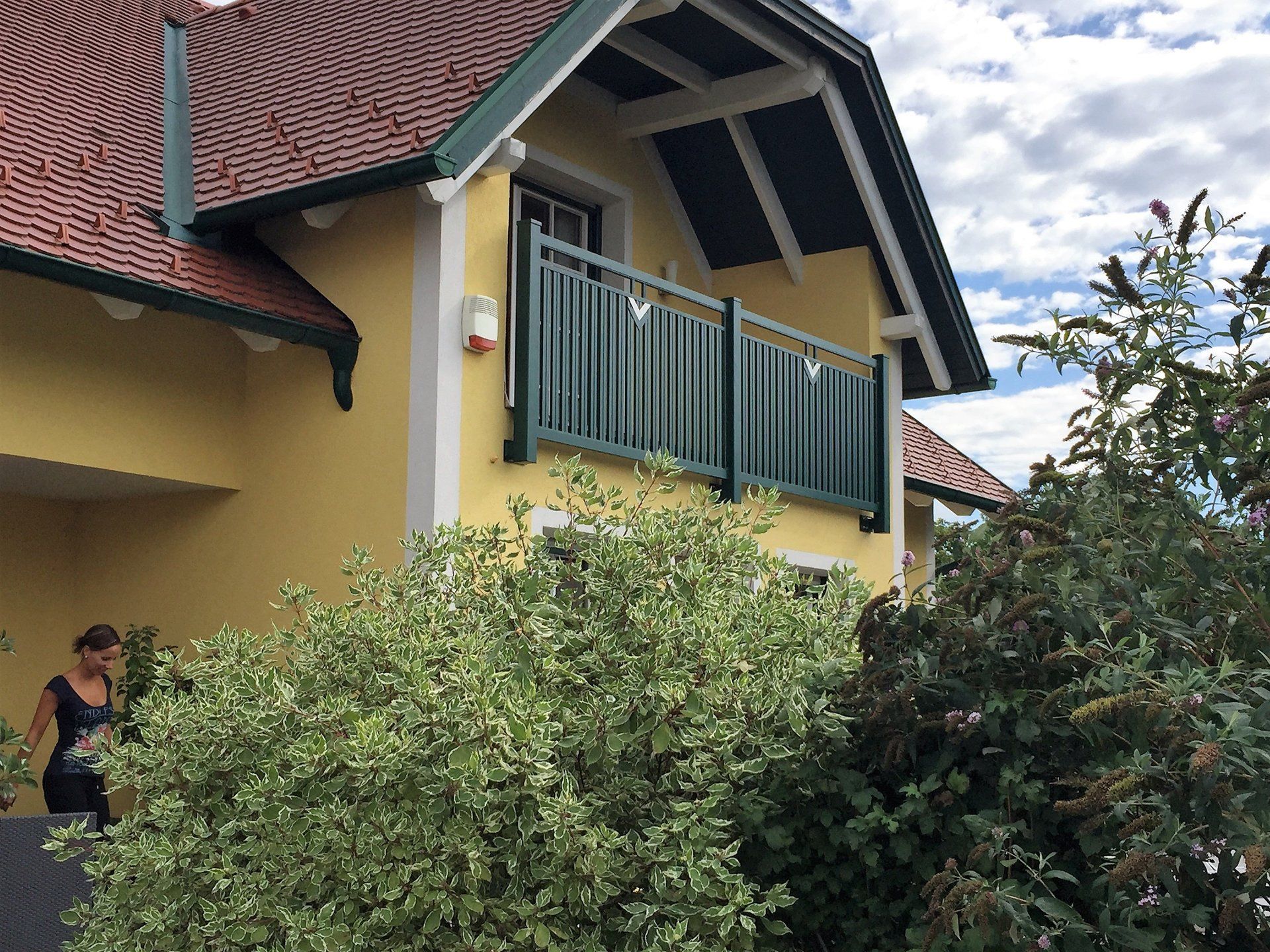 Eine Frau steht vor einem gelben Haus mit einem grünen Balkon.