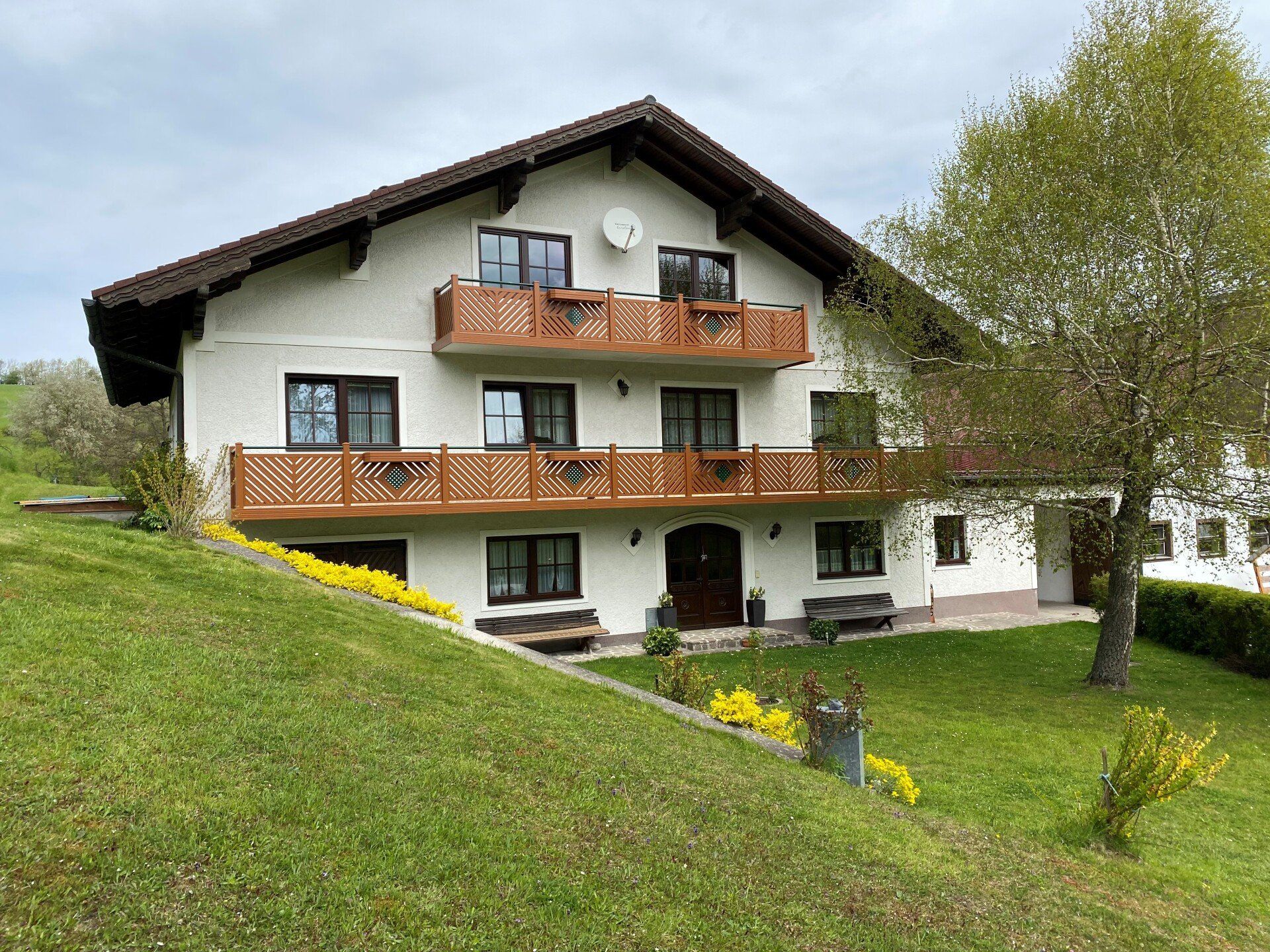 Auf einem grasbewachsenen Hügel steht ein großes weißes Haus mit Balkon.