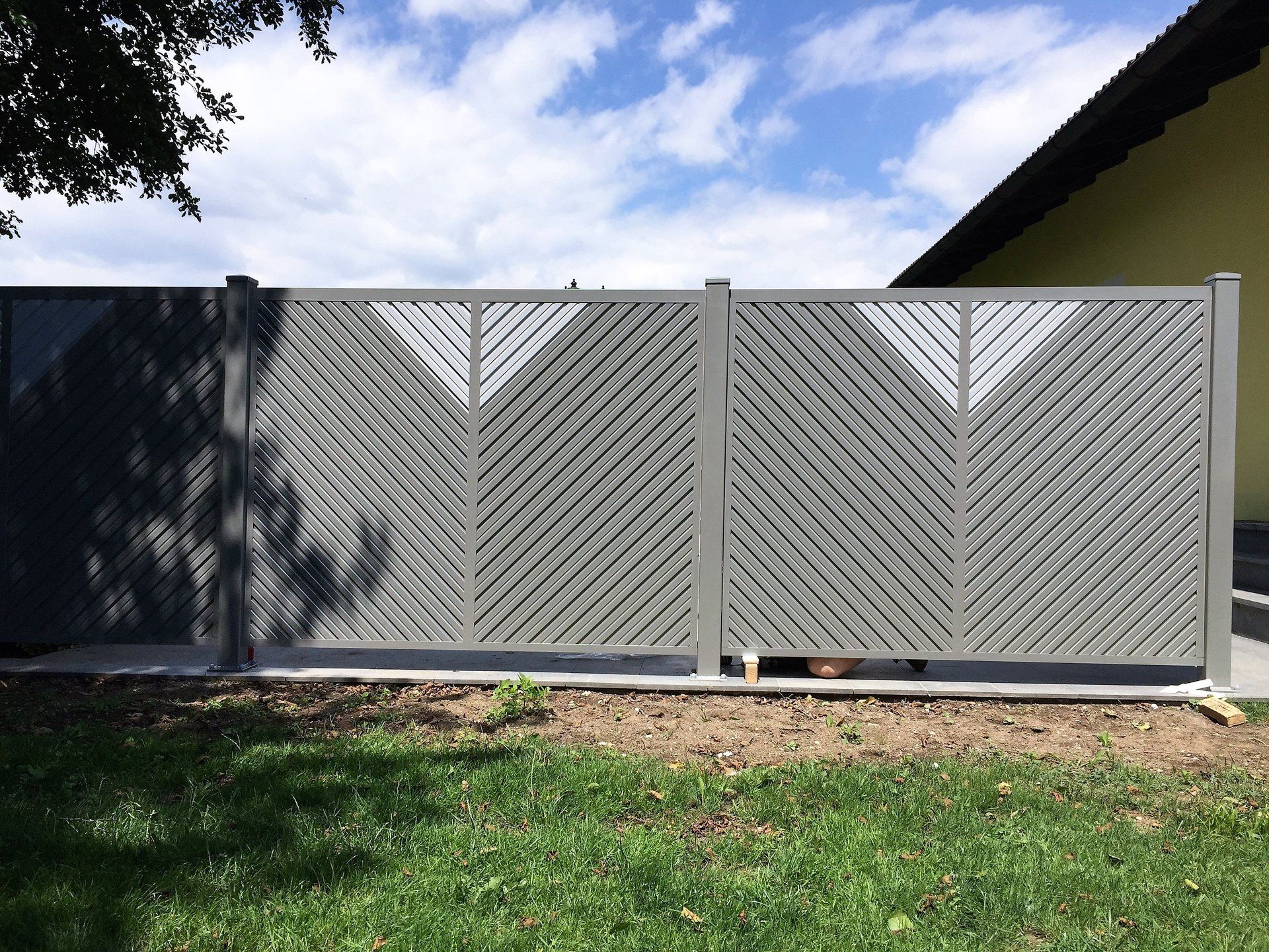 Ein grauer Zaun mit Fischgrätenmuster vor einem Haus