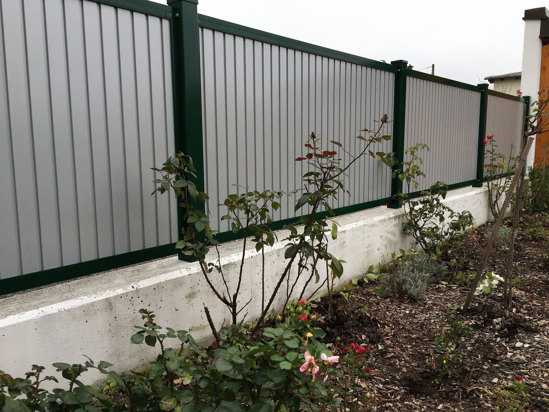 Ein Zaun mit einem grünen Rahmen ist von Blumen in einem Garten umgeben.