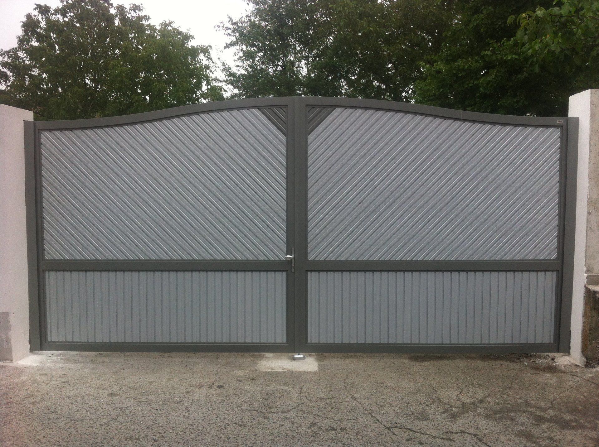 Ein grau-schwarzes Tor mit Bäumen im Hintergrund