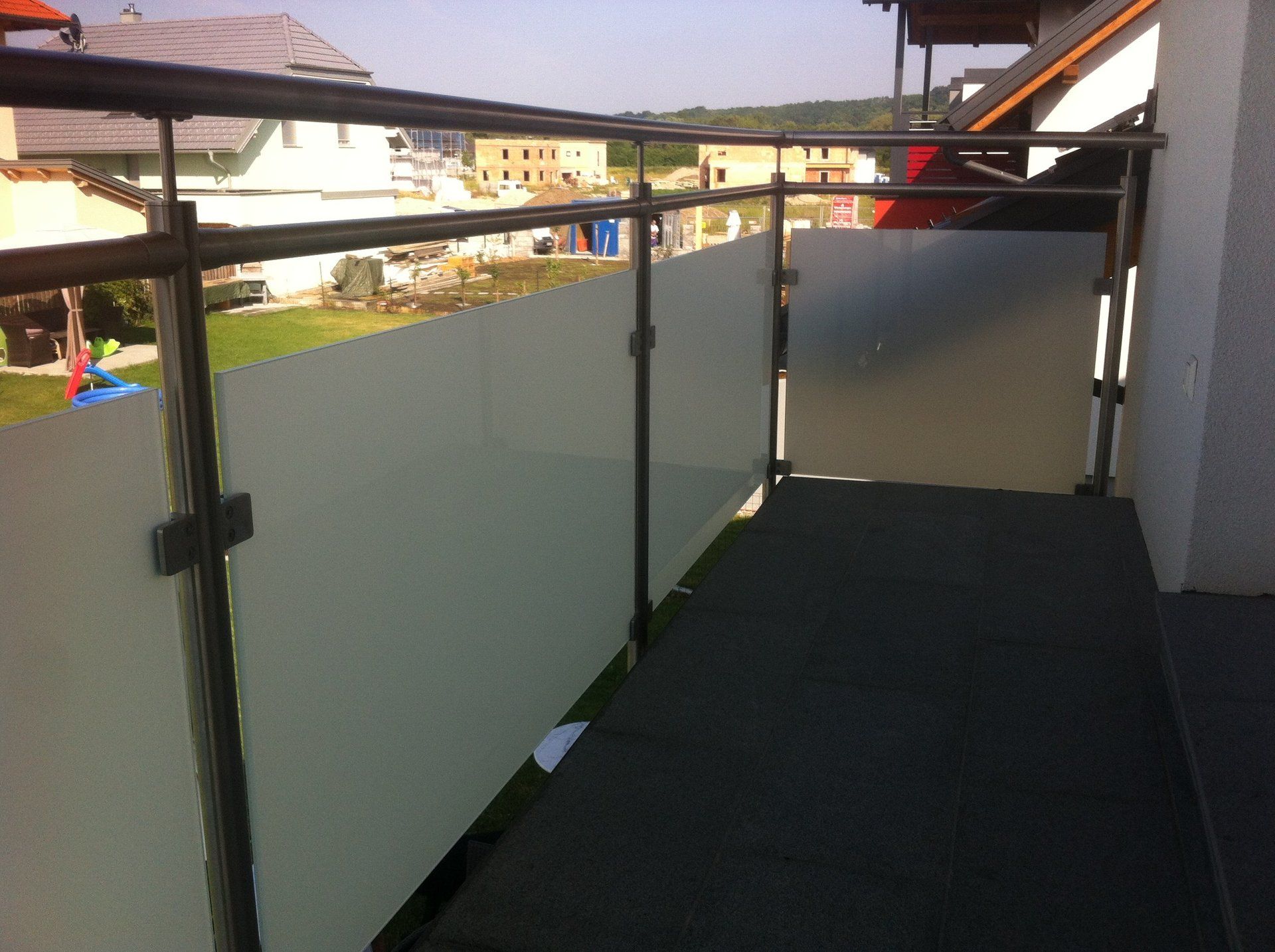 Ein Balkon mit schwarzem Geländer und weißem Glas