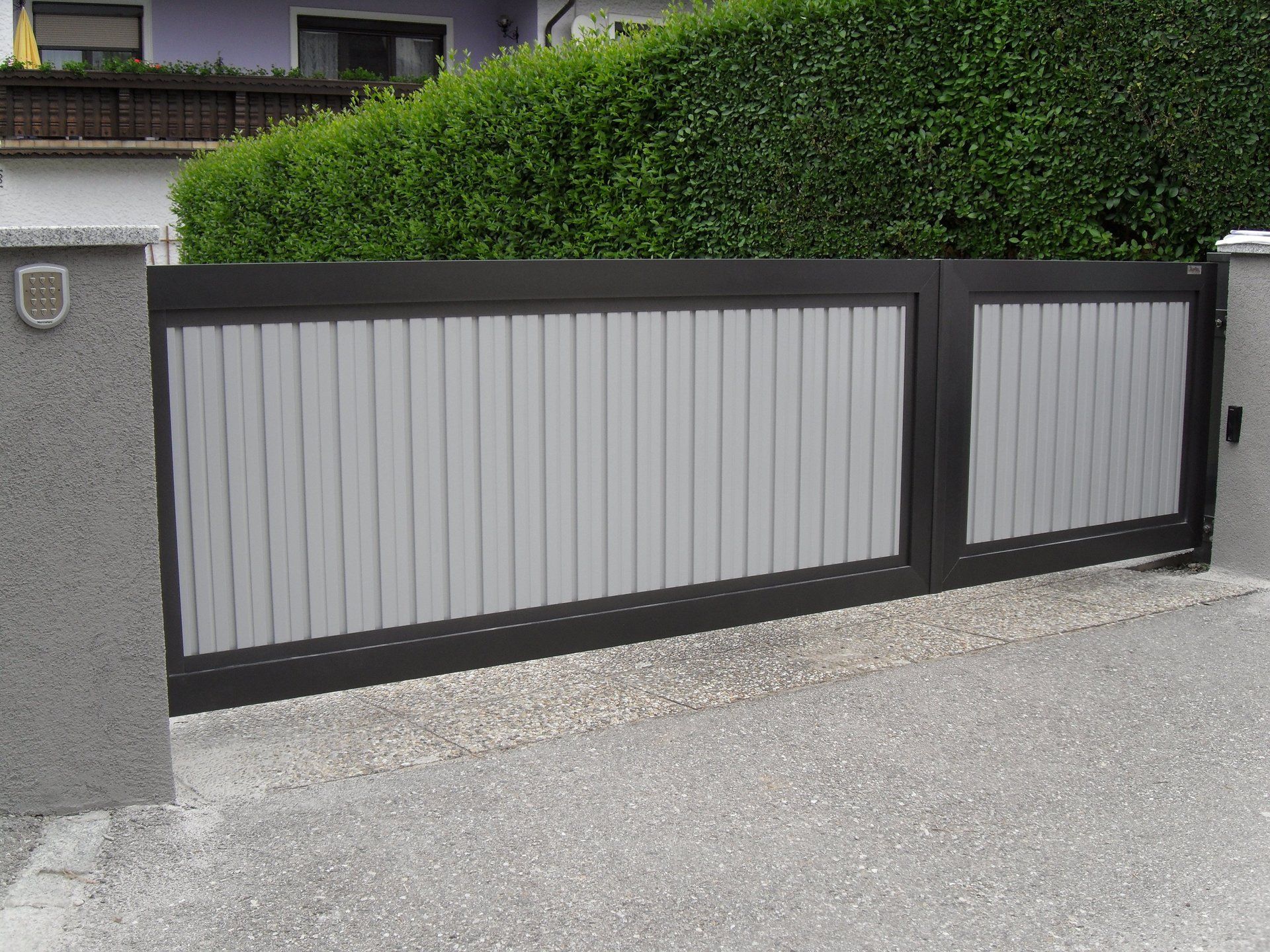 Vor einem Haus steht ein grau-schwarzes Tor.
