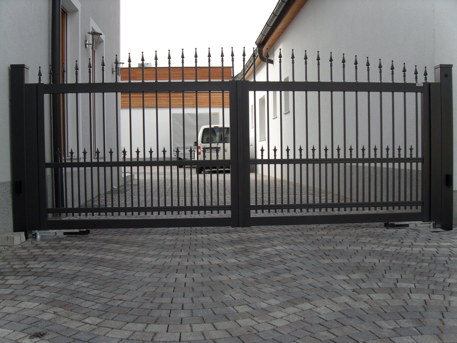 Vor einem weißen Gebäude steht ein schwarzes Tor offen