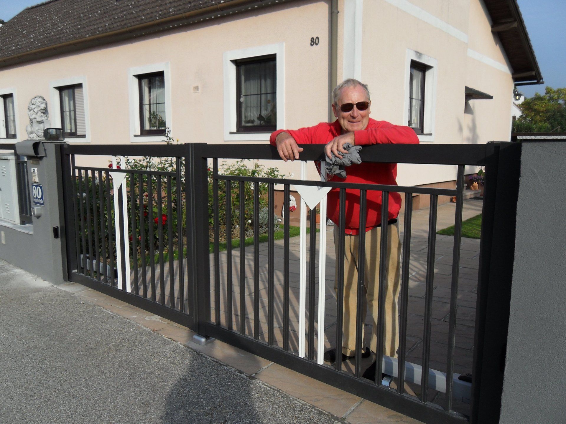 Ein Mann lehnt an einem Zaun vor einem Haus