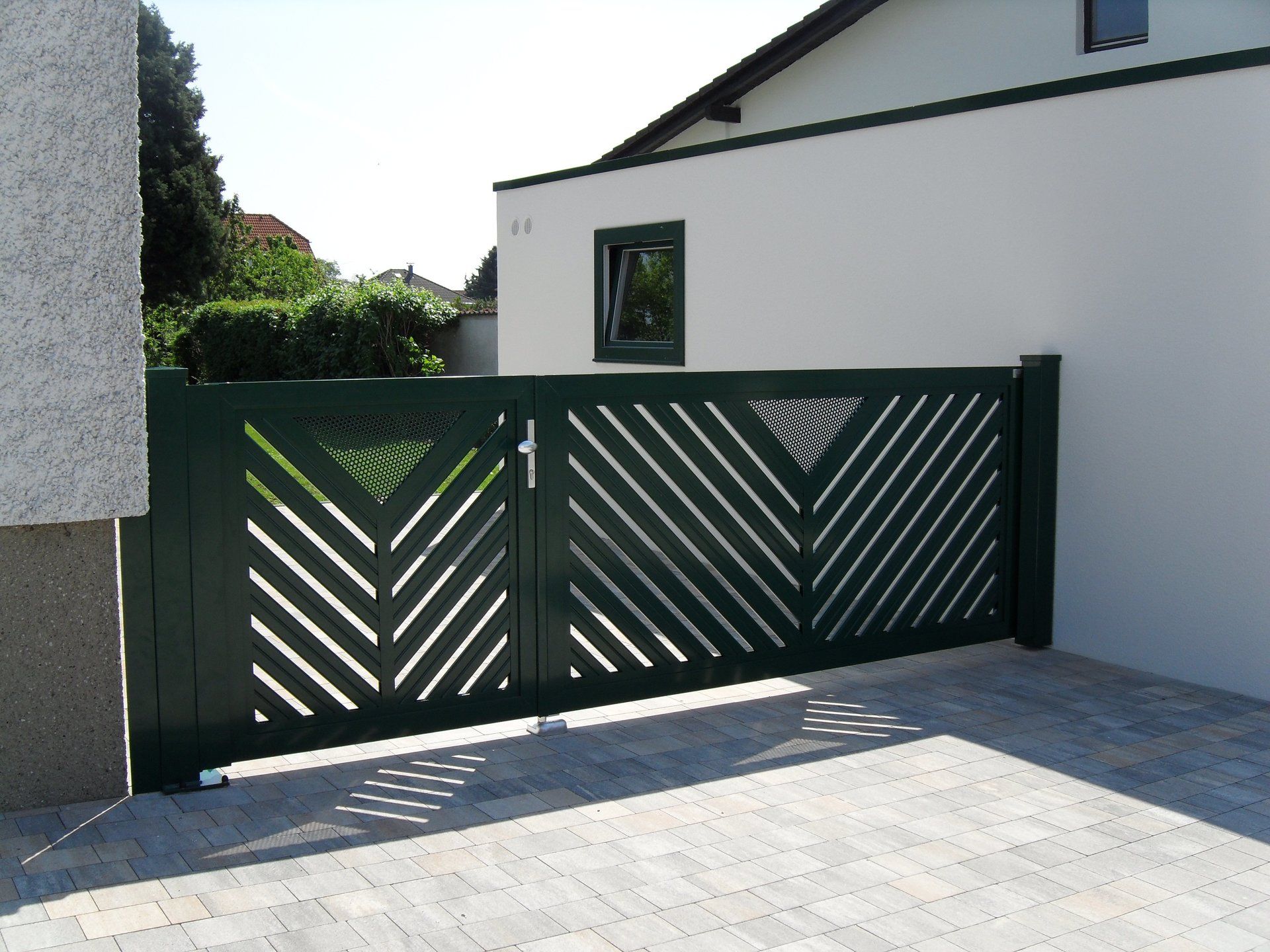 Ein grünes Tor mit geometrischem Muster öffnet sich zu einer Einfahrt