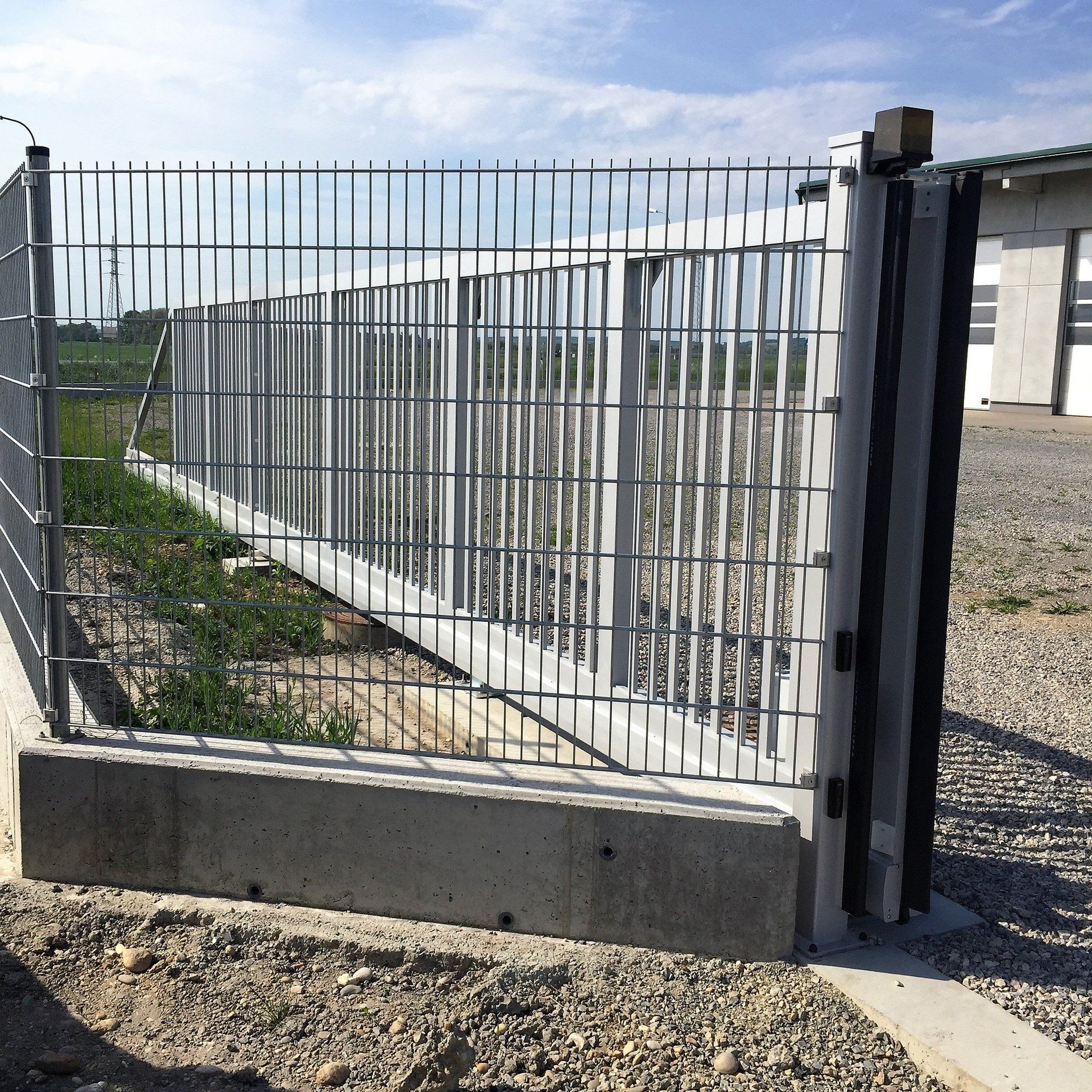 Ein Zaun mit Schiebetor ist von Kies umgeben