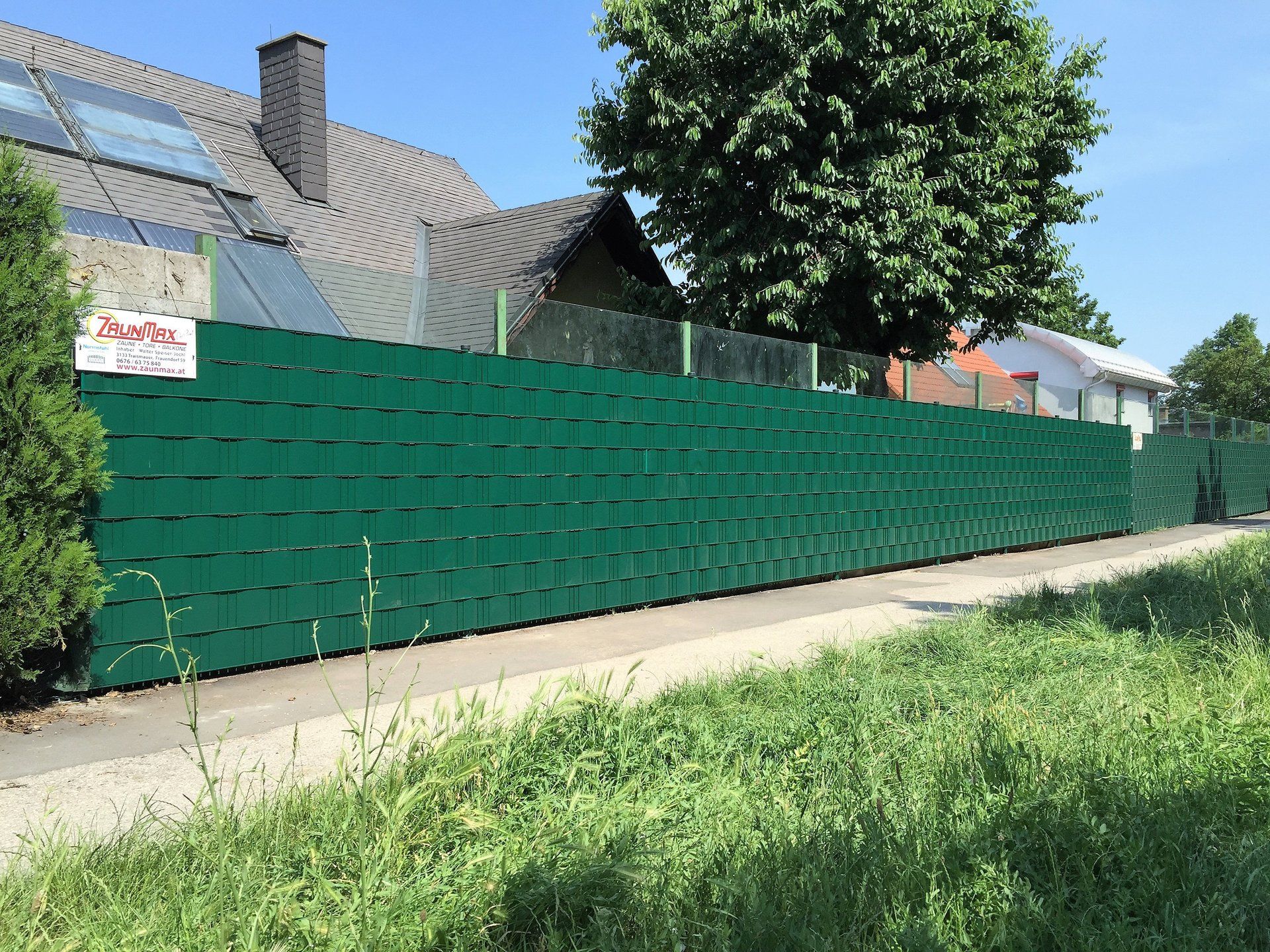 Vor einem Haus ist ein grüner Zaun von Gras und Bäumen umgeben.