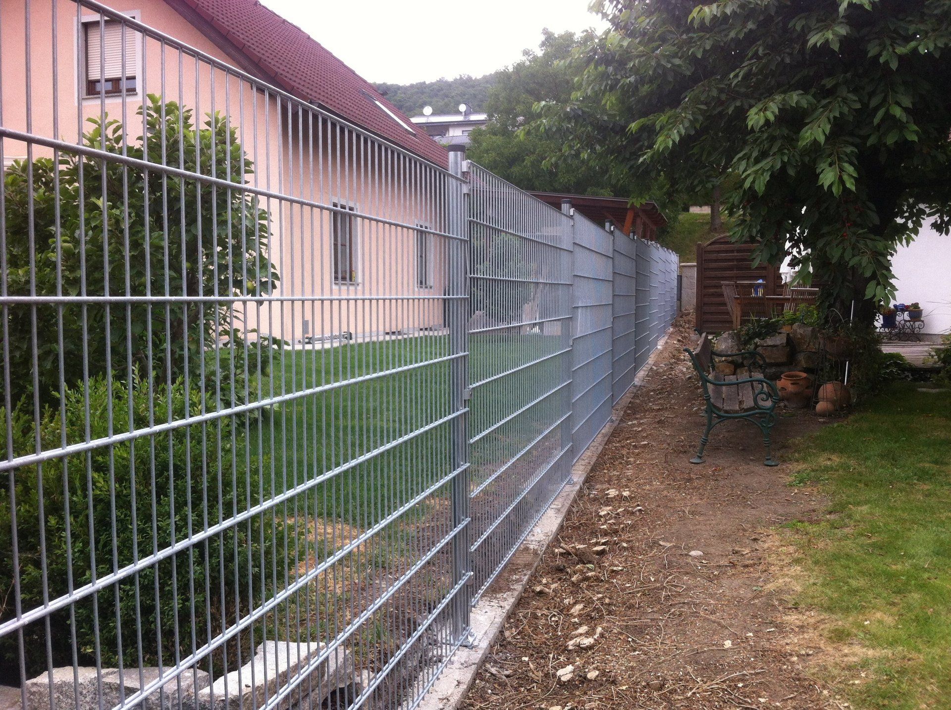 Ein Metallzaun umgibt einen Hof mit einem Haus im Hintergrund