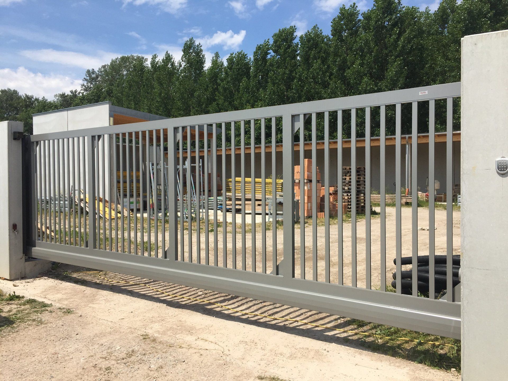 Vor einem Gebäude ist ein Schiebetor geöffnet, im Hintergrund sind Bäume zu sehen.