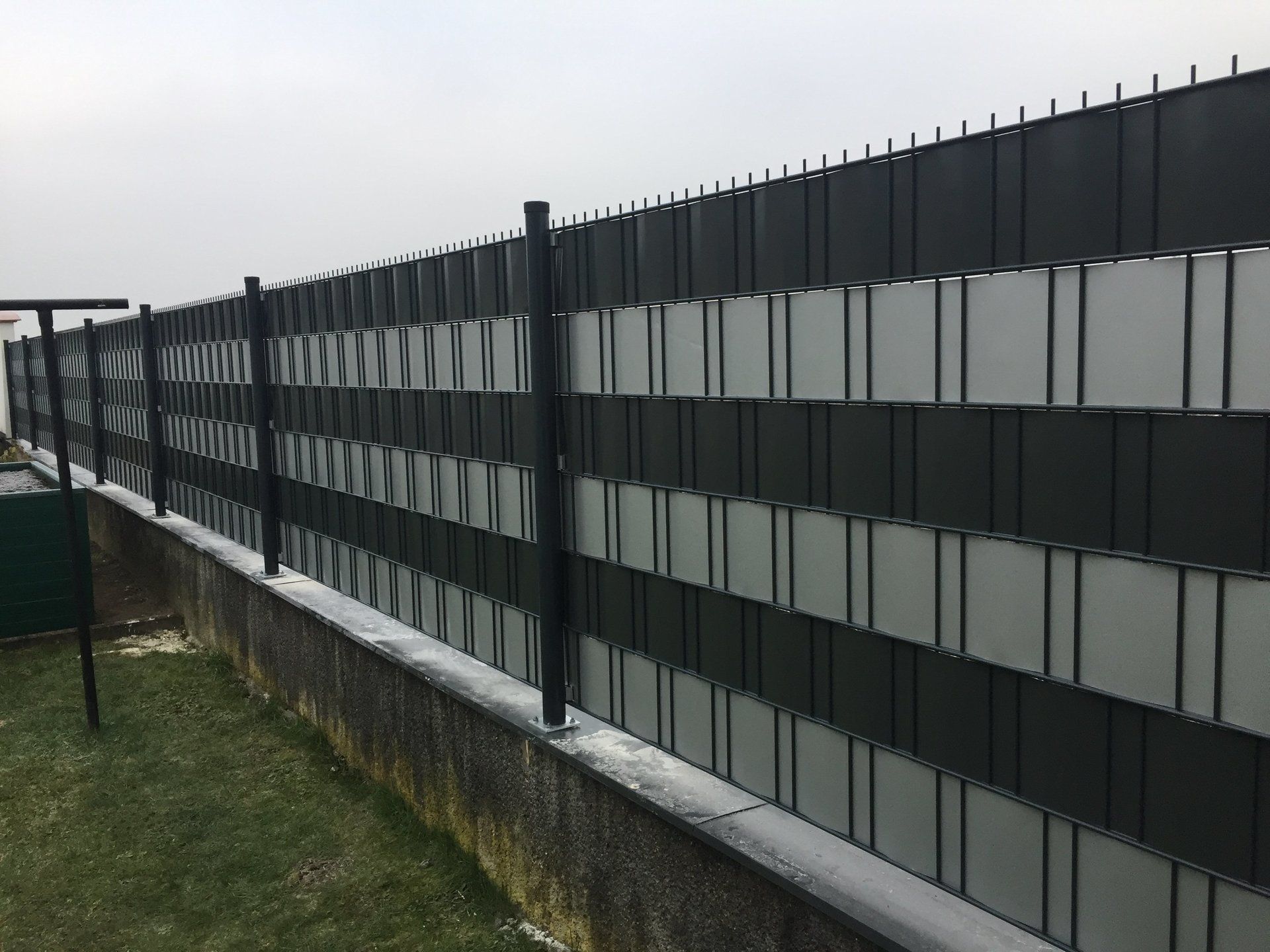 Auf einer Betonmauer steht ein schwarz-weißer Zaun.