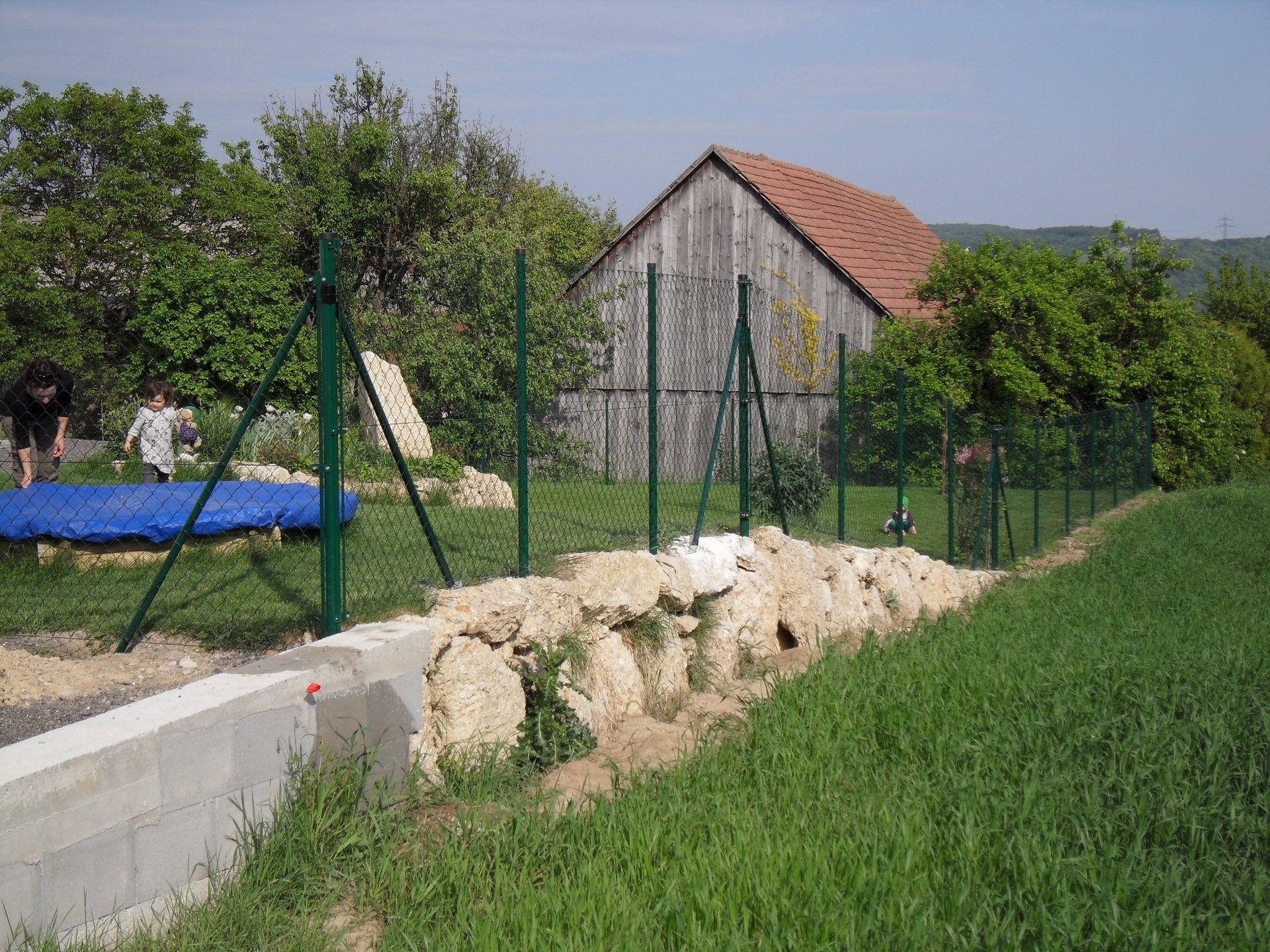 Ein eingezäunter Hof mit einem Trampolin und einer Scheune im Hintergrund