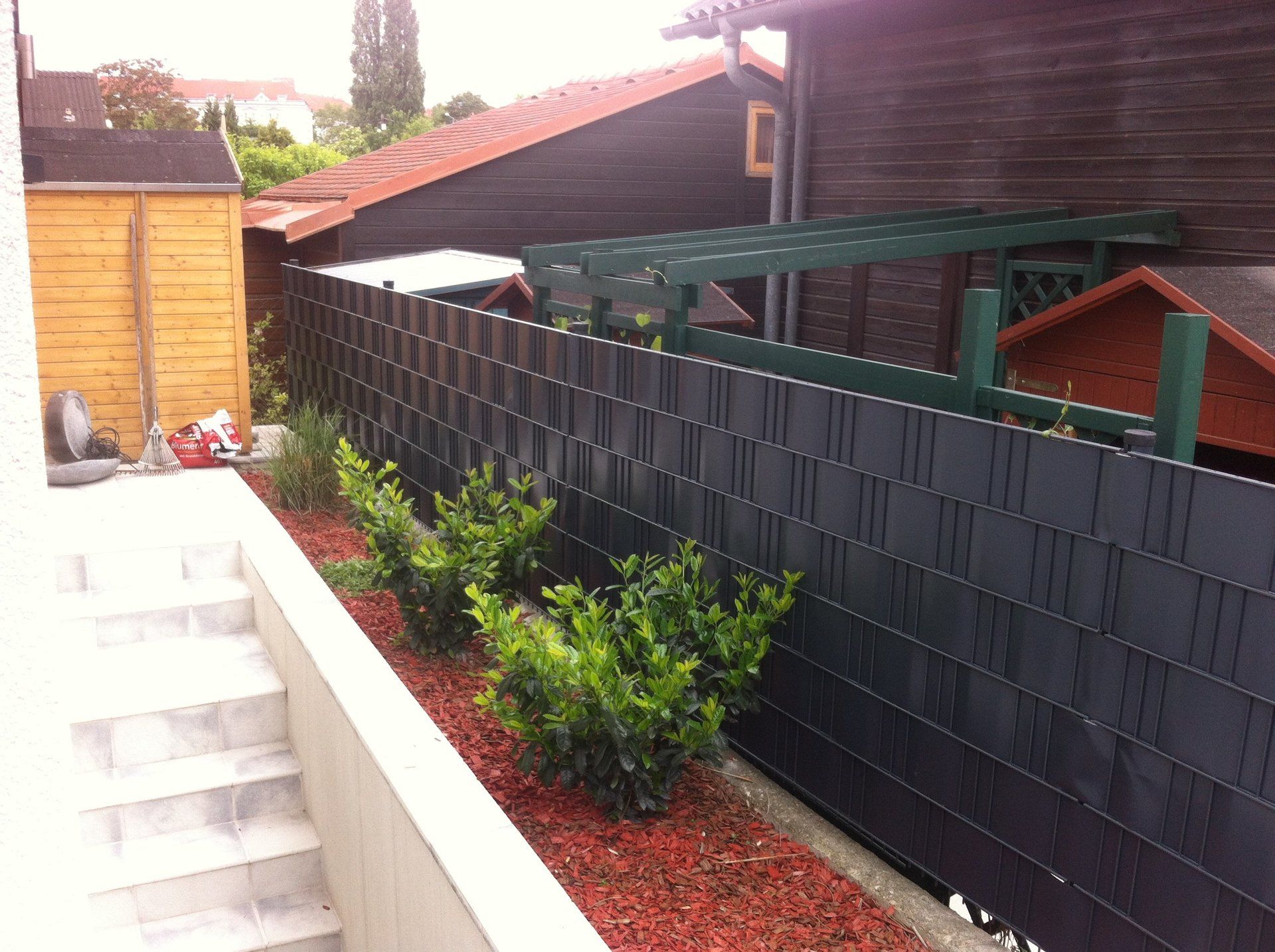 Ein schwarzer Zaun umgibt einen Garten mit Treppen im Hintergrund