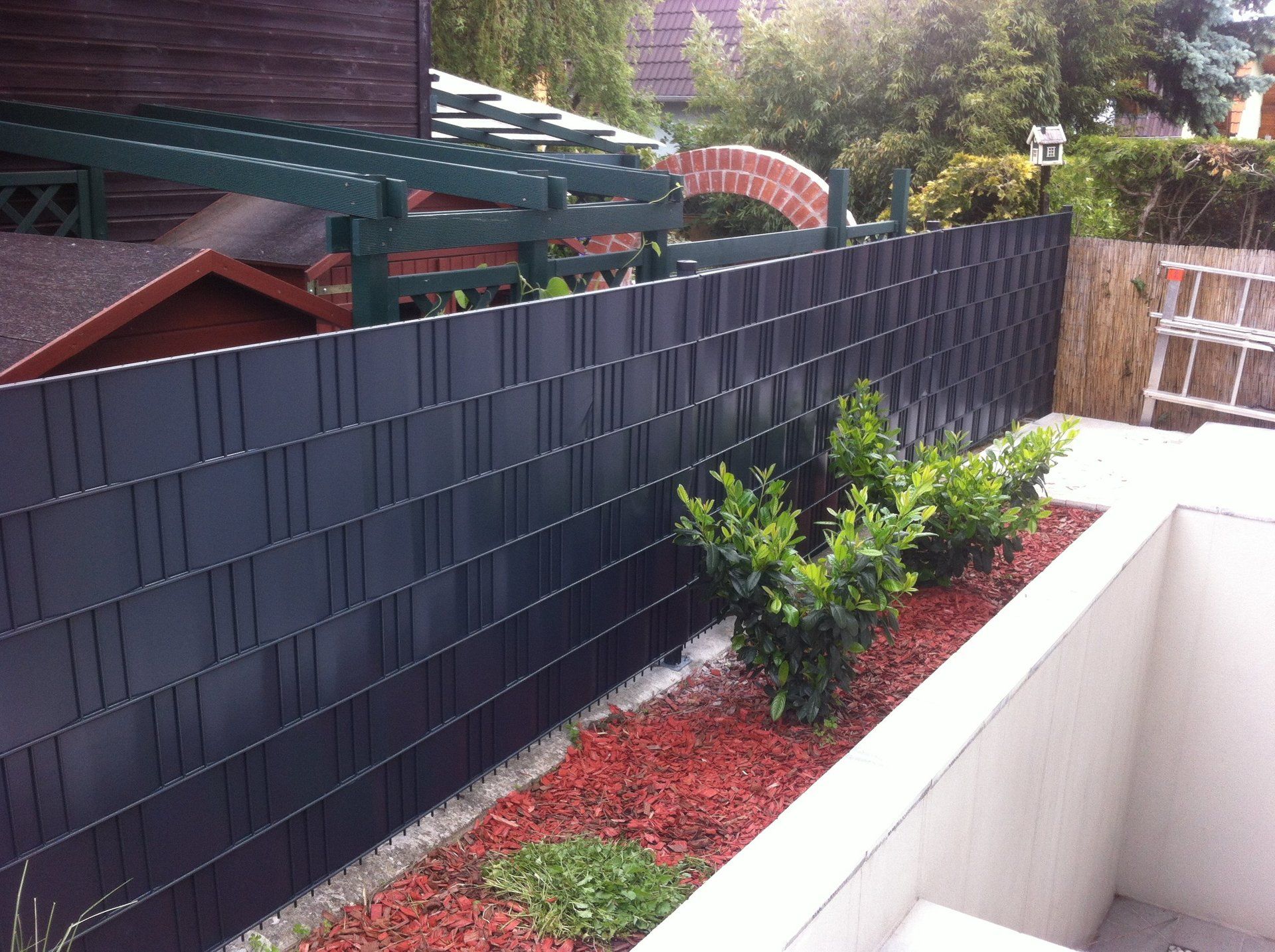 Ein schwarzer Zaun umgibt einen Garten mit einem Schuppen im Hintergrund