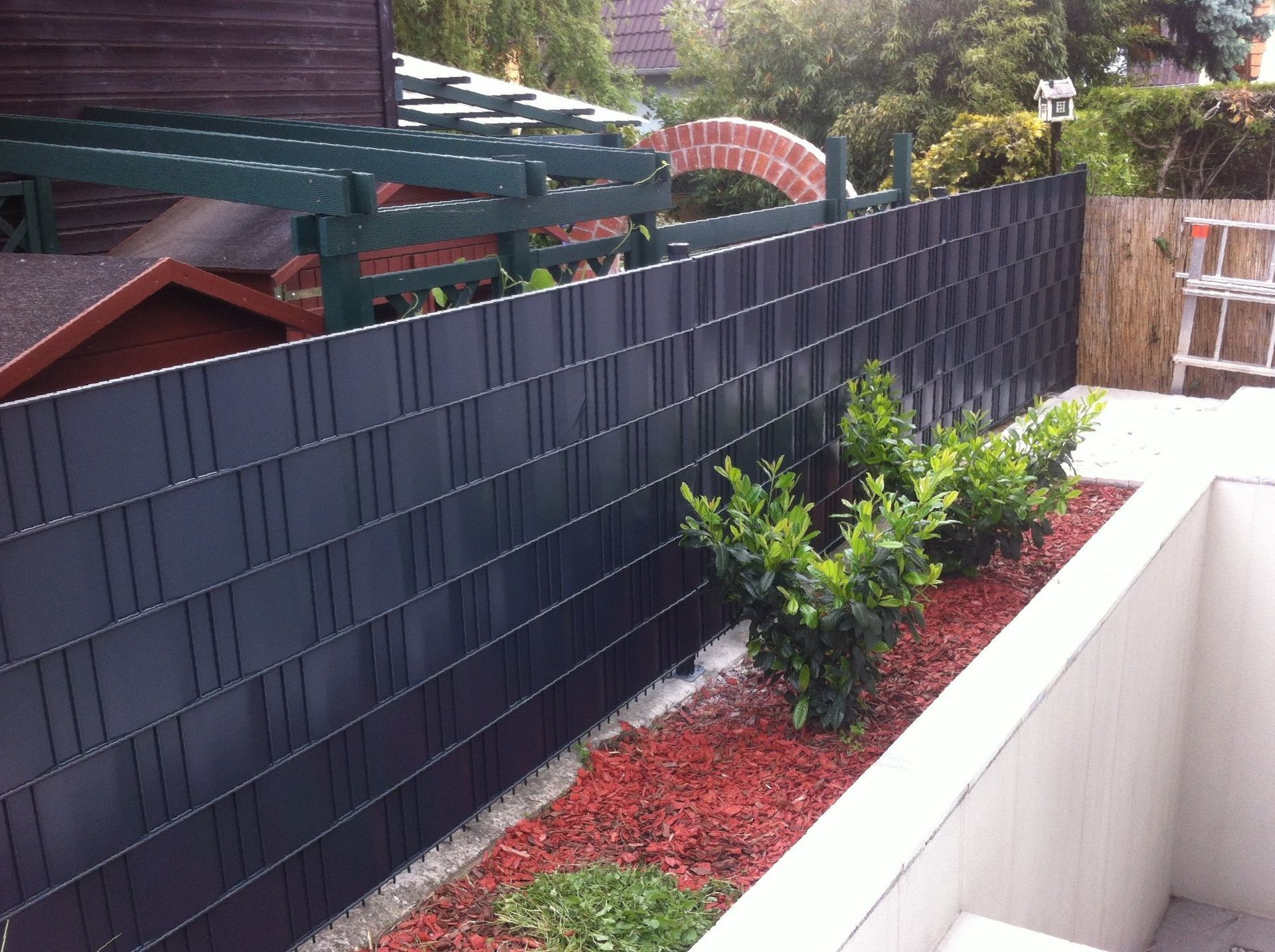 Ein schwarzer Zaun umgibt einen Garten mit Pflanzen und Mulch.