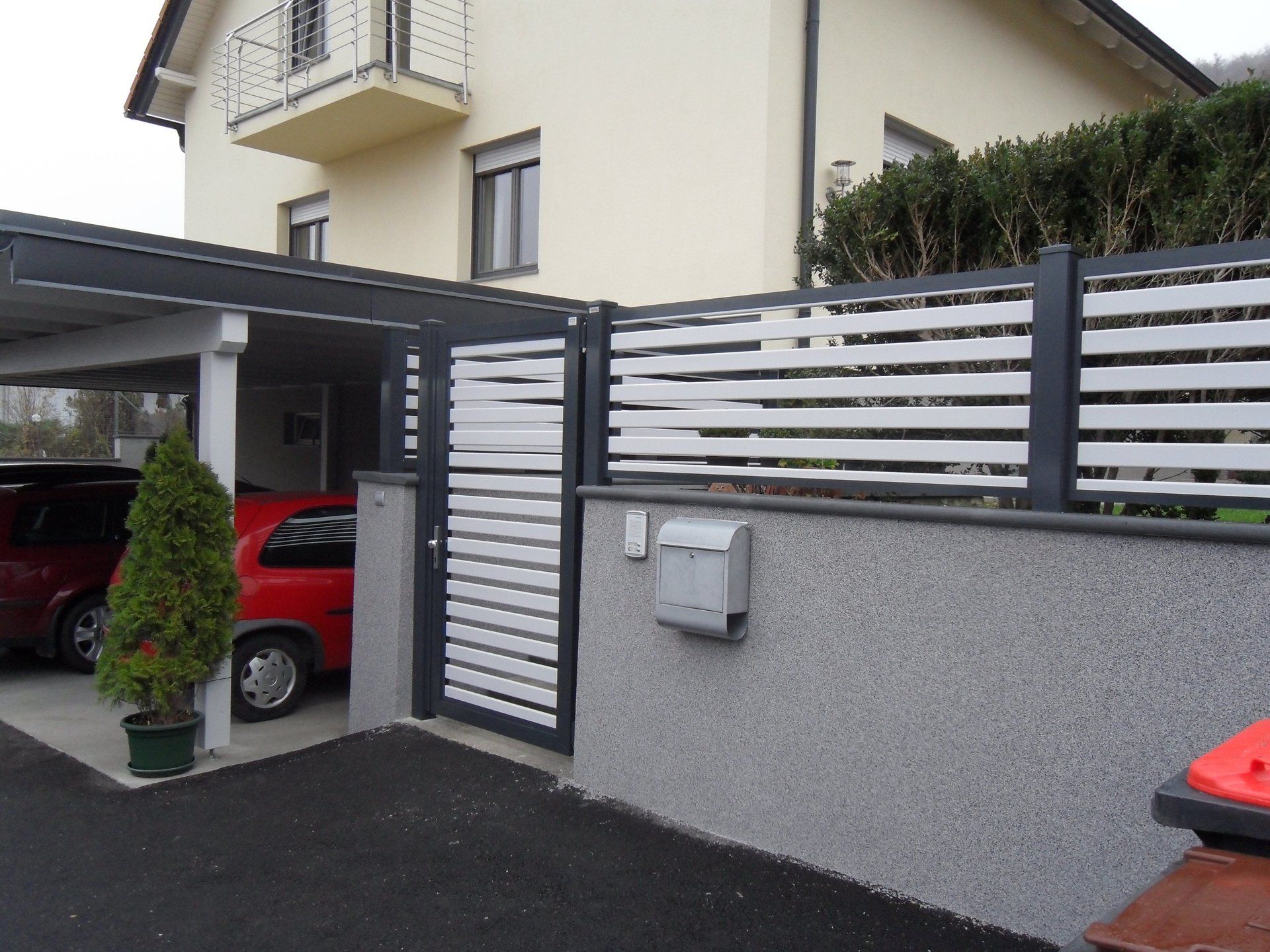 Ein rotes Auto ist unter einem Vordach vor einem Haus geparkt