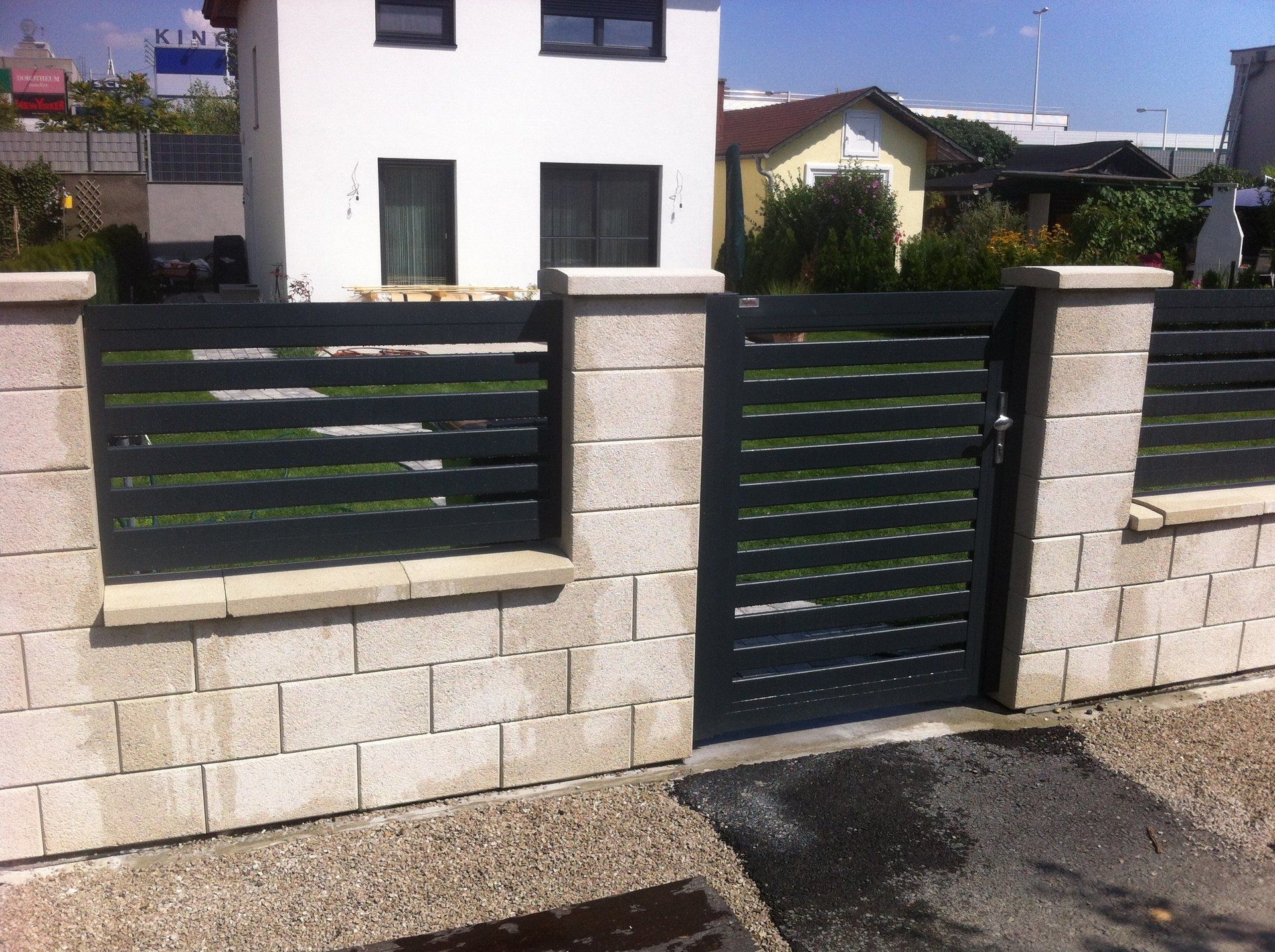 Ein Ziegelzaun mit einem schwarzen Tor vor einem Haus