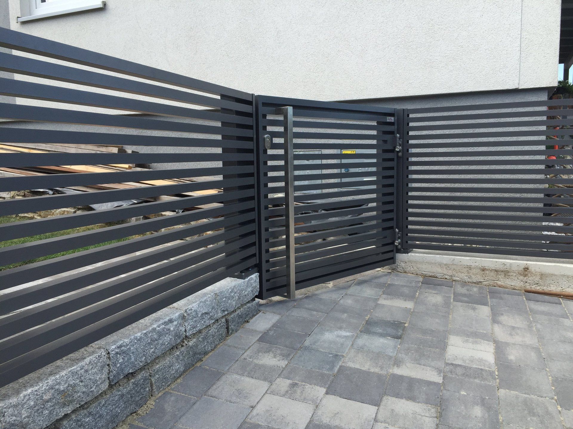 Ein schwarzer Metallzaun mit einem Tor vor einem Haus.