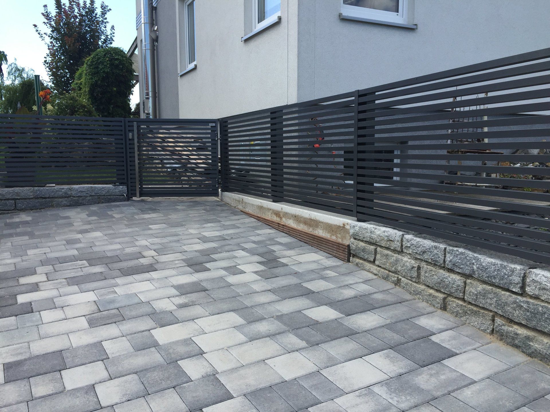 Ein Zaun umgibt eine gepflasterte Auffahrt vor einem Haus.