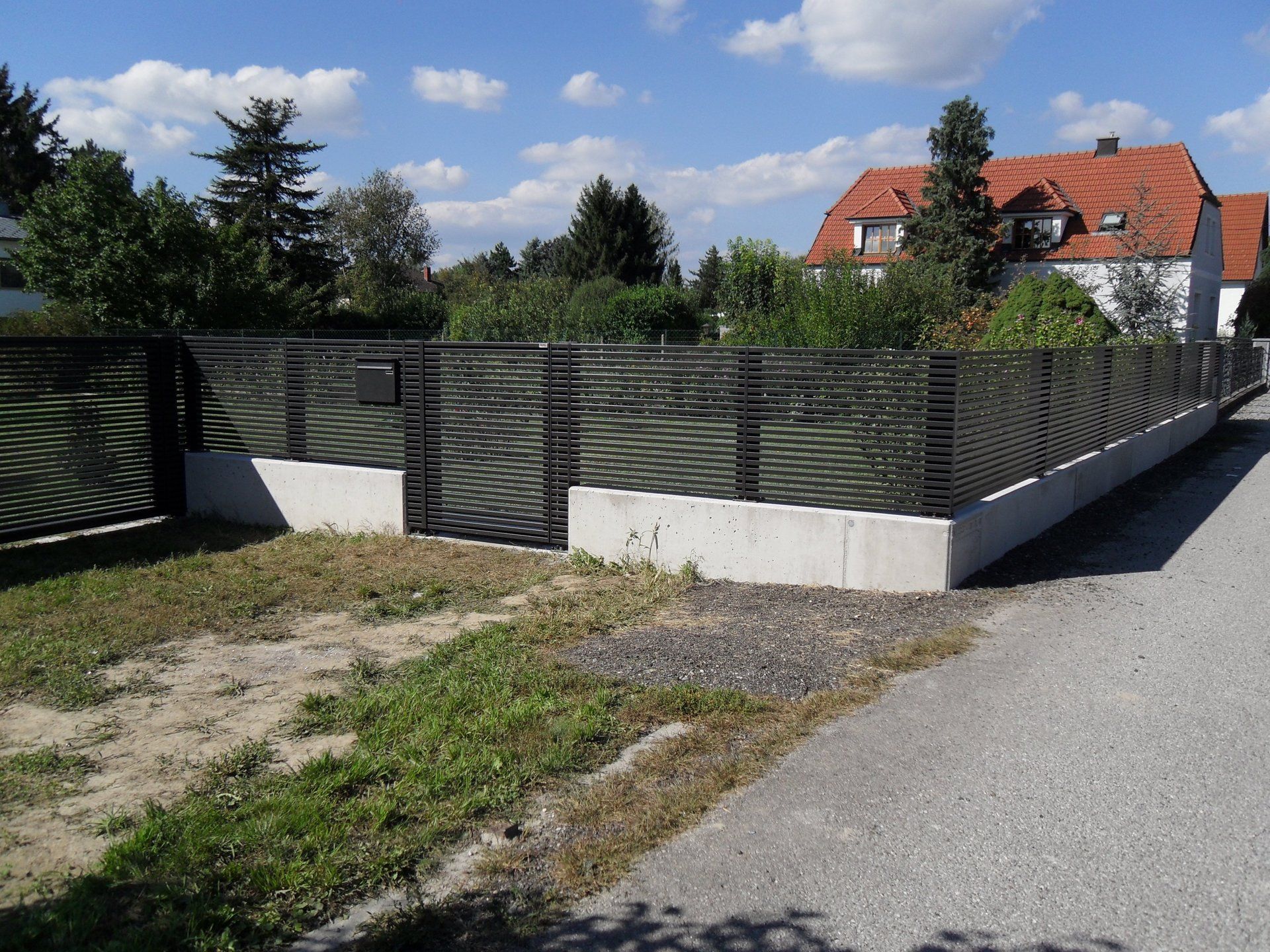 Ein Zaun am Straßenrand mit einem Haus im Hintergrund