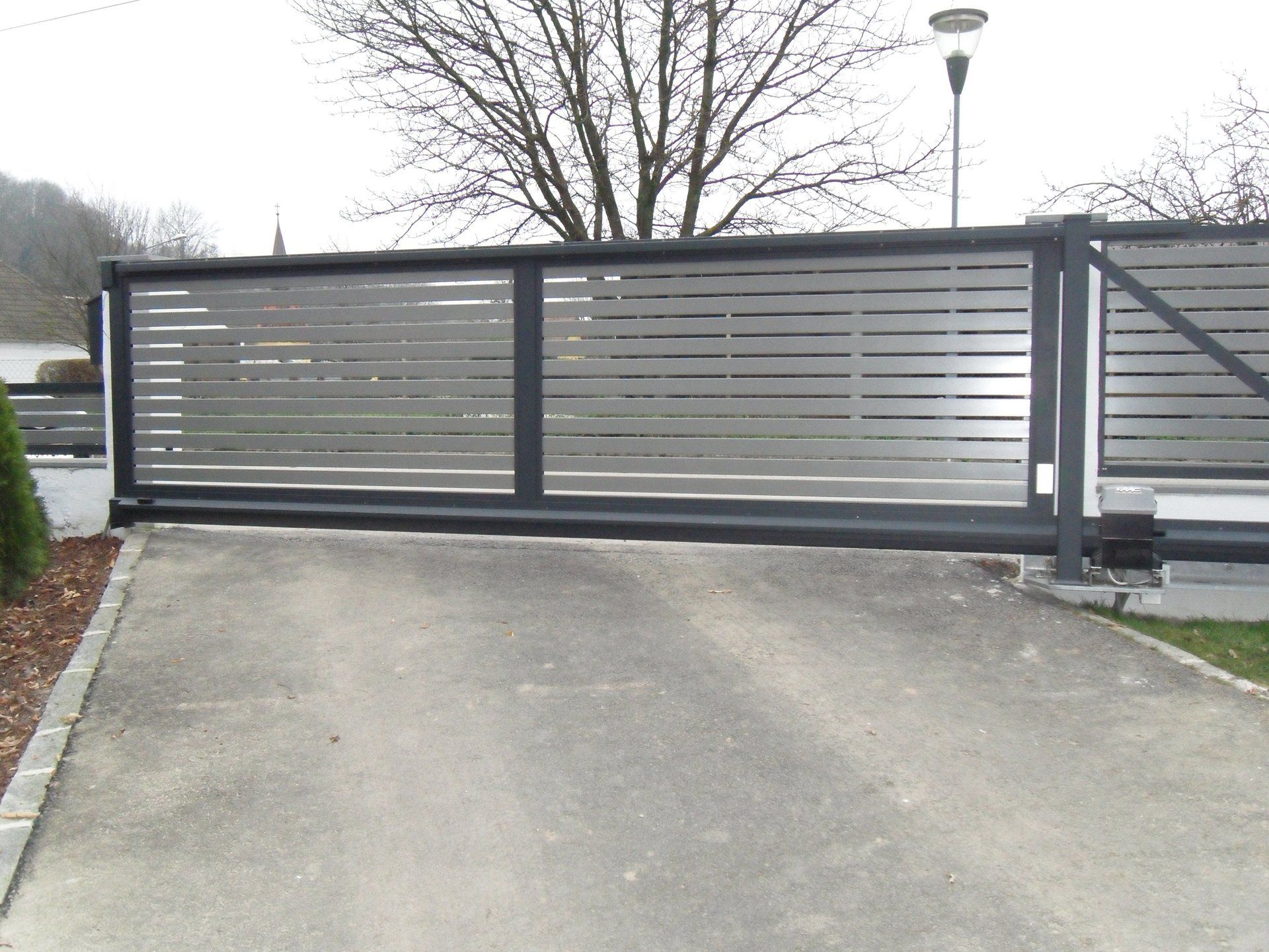Ein Schiebetor auf einer Einfahrt mit einem Baum im Hintergrund