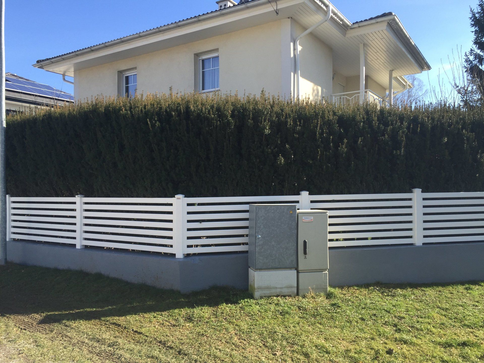 Ein weißer Zaun umgibt ein Haus mit einer Hecke dahinter