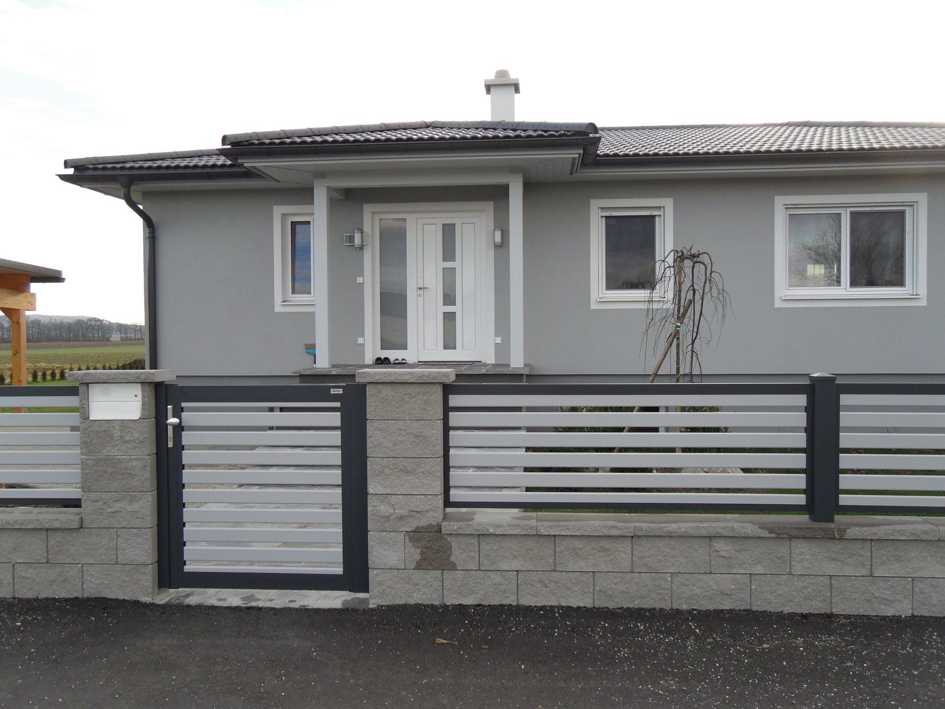 Ein graues Haus mit einer weißen Tür und einem weißen Zaun