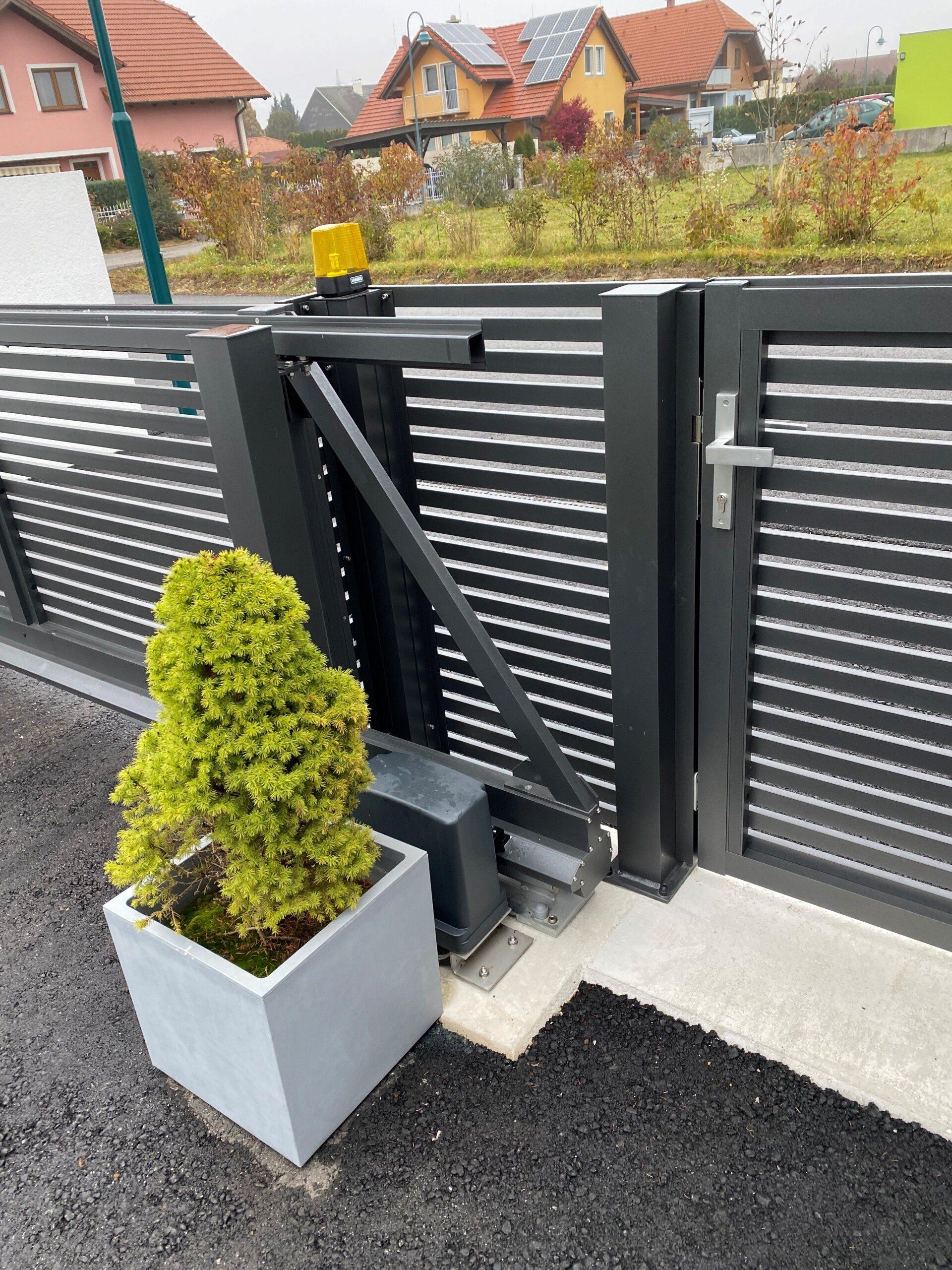 Neben einem Schiebetor steht eine Topfpflanze.