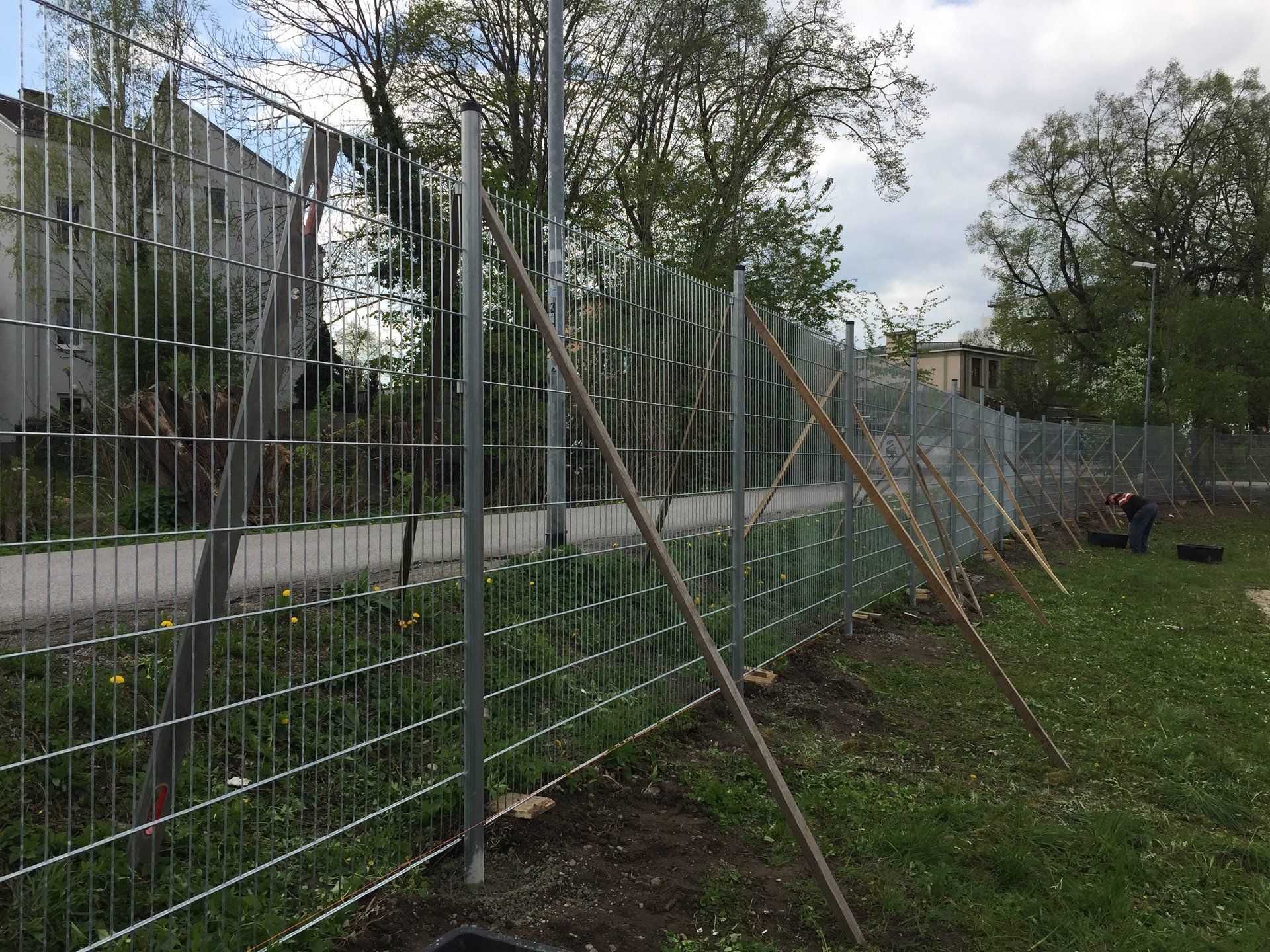 In einem Park mit Bäumen im Hintergrund wird ein Zaun gebaut.