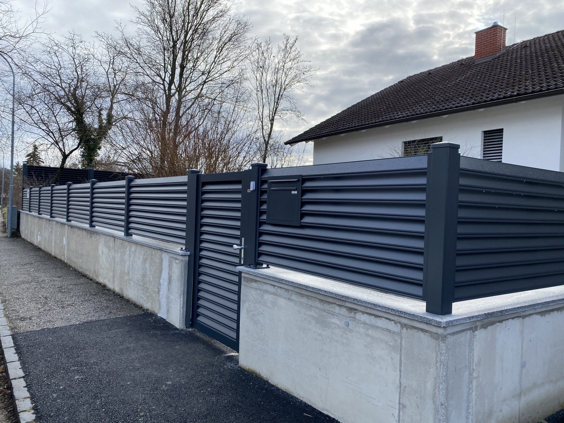 Ein schwarzer Zaun mit einem Briefkasten vor einem Haus.