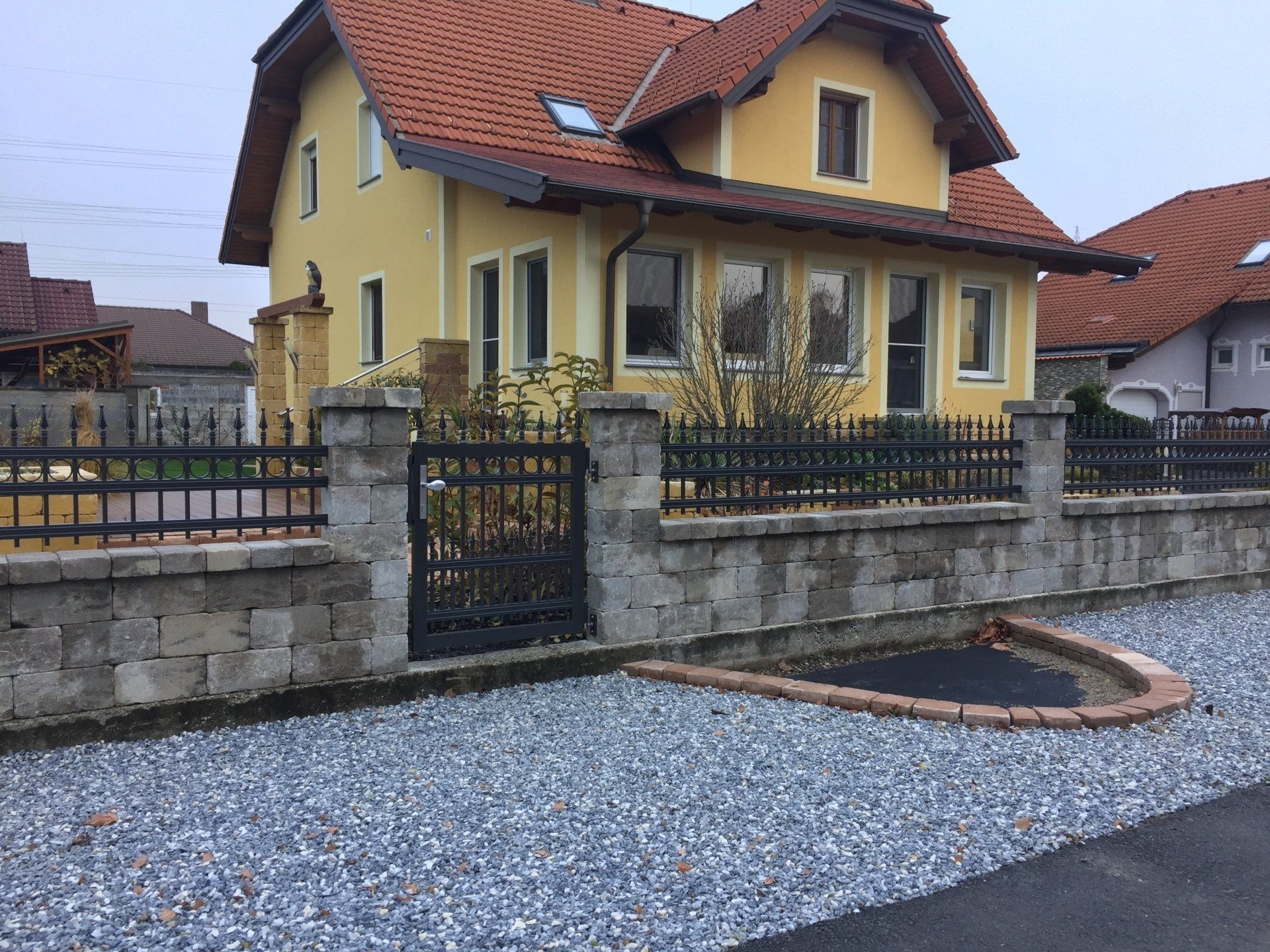 Ein gelbes Haus mit einem schwarzen Zaun und Kies davor